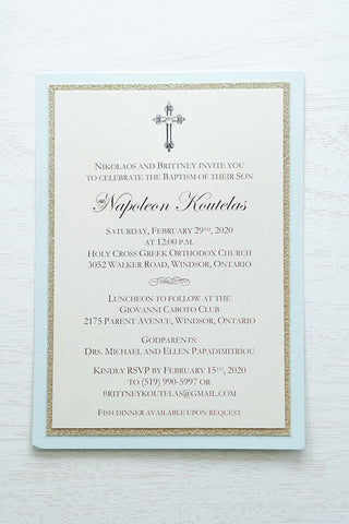 alt=“Classic layered Baptism invitation features an ivory pearlescent shimmer card stock on a gold glitter and soft blue pearlescent shimmer card stock and an elegant cross and jewel detail”