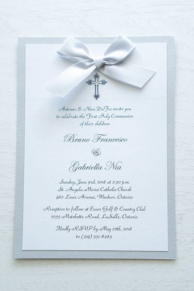 alt=“Classic embellished First Communion invitation features a white pearlescent shimmer card stock on silver pearlescent shimmer card stock, an elegant cross and jewel detail finished with a rich silver satin ribbon bow”