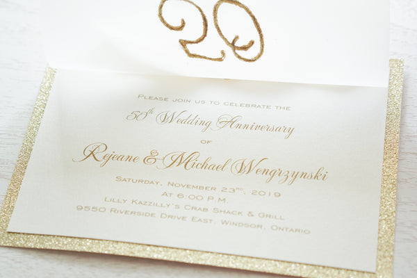 alt=“Elegant 50th Wedding Anniversary invitation features a vellum layer on ivory pearlescent shimmer and gold glitter card stock, an elegant gold glitter 50th sparkle detail and is finished together with a rich ivory satin ribbon bow”