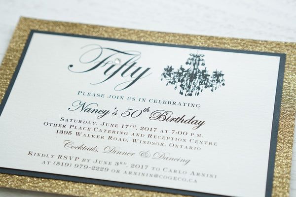 alt="Elegant birthday invitation features an ivory pearlescent shimmer card stock on matte black and gold glitter card stock, a beautiful chandelier image, fifty written in script and is finished with a jewel detail"