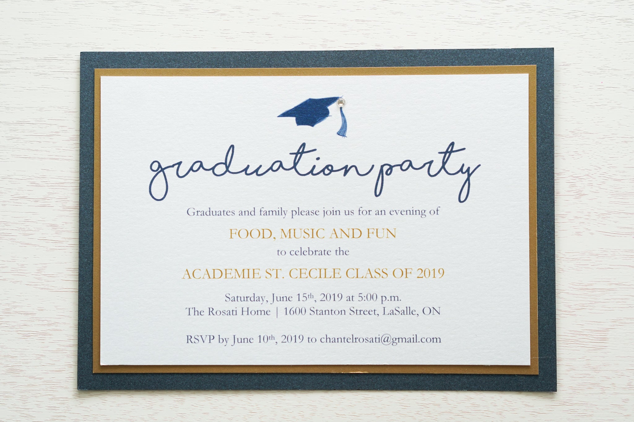 alt="Classic graduation party invitation features a white pearlescent shimmer stock on gold leaf and navy blue pearlescent shimmer card stock layers, a blue grad cap and jewel detail and a modern script font"