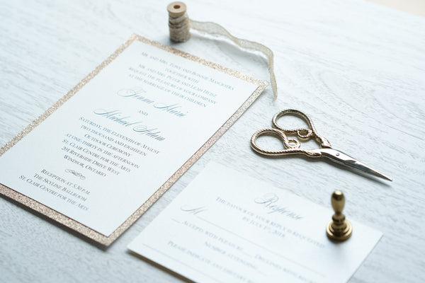 alt="Classic wedding invitation features an ivory pearlescent shimmer card stock layered onto rose gold glitter and an elegant script font"