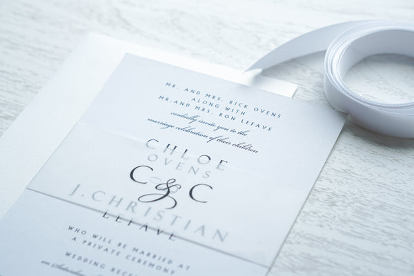 alt="Modern wedding invitation features a white matte card stock, black script and block font and a vellum belly band with monogram detail"