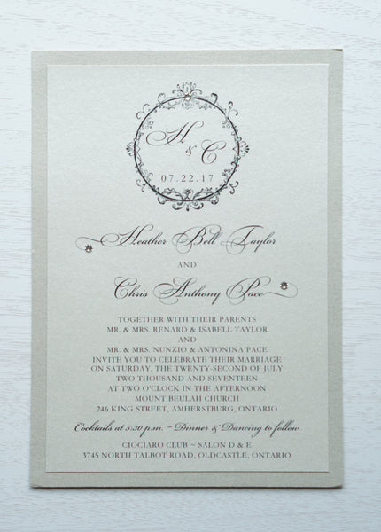 alt="Timeless wedding invitation features an ivory pearlescent shimmer card stock on a champagne gold pearlescent shimmer stock, an elegant script font and a round frame design with a monogram/jewel detail"