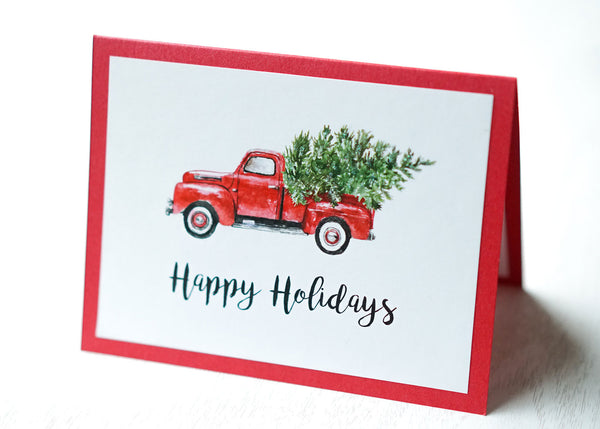 alt="This vintage card features a white matte card stock on a red pearlescent shimmer card stock, a vintage red truck with tree and glitter dust and “Happy Holidays” or "Merry Christmas” in a black script font"