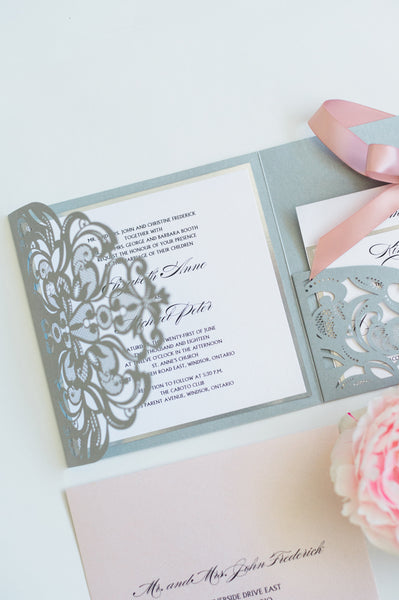 alt="Elegant silver pearlescent shimmer laser cut square pocket fold wedding invitation features a white pearlescent shimmer stock on a silver mirror stock and is tied together with a rich pink satin ribbon bow"