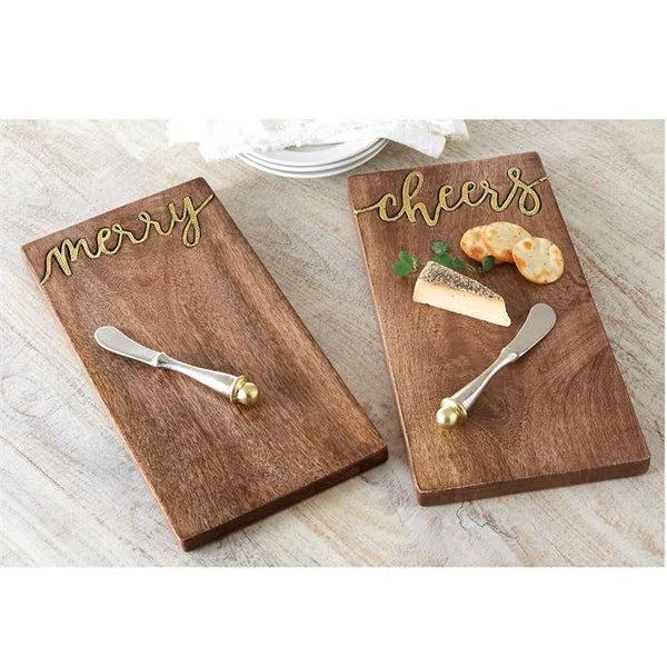 alt="Mango wood serving board features hammered gold metal "cheers" inset. Arrives with hammered metal spreader with capped gold accent"