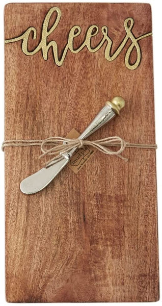 alt="Mango wood serving board features hammered gold metal "cheers" inset. Arrives with hammered metal spreader with capped gold accent"