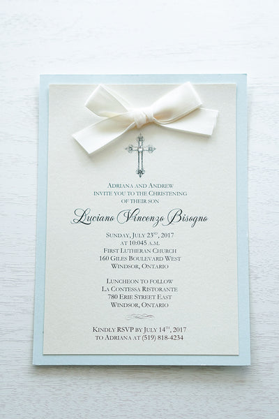 alt="Classic Baptism invitation with ivory pearescent shimmer card stock mounted onto a soft blue  pearlescent shimmer cardstock, a rich ivory satin bow and an elegant cross and jewel detail"