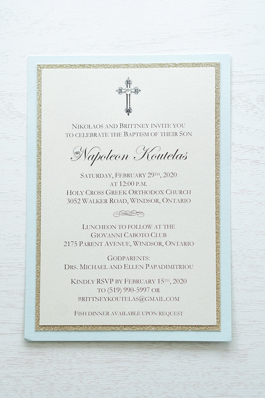 alt=“Classic layered Baptism invitation features an ivory pearlescent shimmer card stock on a gold glitter and soft blue pearlescent shimmer card stock and an elegant cross and jewel detail”