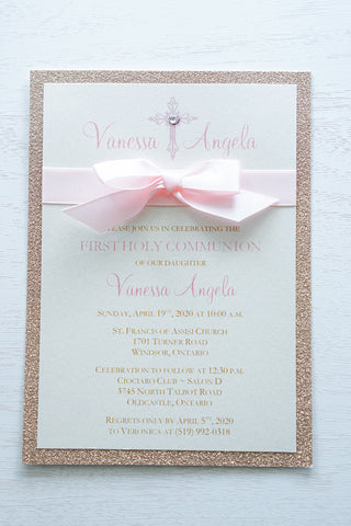 alt=“Sweet glitter First Communion invitation with an ivory pearlescent shimmer card stock on a rose gold glitter stock, a rich pink satin ribbon and bow and an elegant pink cross and jewel detail with the honouree’s name”