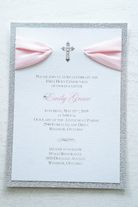 alt="Elegant silver glitter First Communion invitation features a white pearlescent shimmer card stock on a silver glitter stock, a rich pink satin ribbon and an elegant cross and jewel detail"