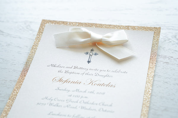 alt=“Classic embellished Baptism invitation features a soft pink pearlescent shimmer card stock on a rose gold glitter card stock, an elegant cross and jewel detail finished with a rich ivory satin ribbon bow”