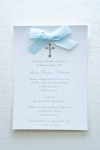 alt=“Classic embellished Baptism invitation features a white pearlescent shimmer card stock, an elegant cross and jewel detail finished with a rich baby blue satin ribbon bow” 