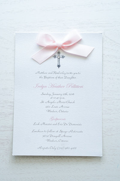 “Classic embellished Baptism invitation features a white pearlescent shimmer card stock, an elegant cross and jewel detail finished with a rich baby pink satin ribbon bow” 