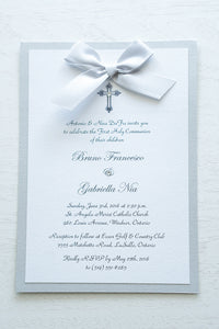 alt=“Classic embellished First Communion invitation features a white pearlescent shimmer card stock on silver pearlescent shimmer card stock, an elegant cross and jewel detail finished with a rich silver satin ribbon bow”