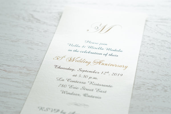 alt=“Simplistic 50th Wedding Anniversary invitation features an ivory pearlescent shimmer card stock and an elegant gold monogram and jewel detail”