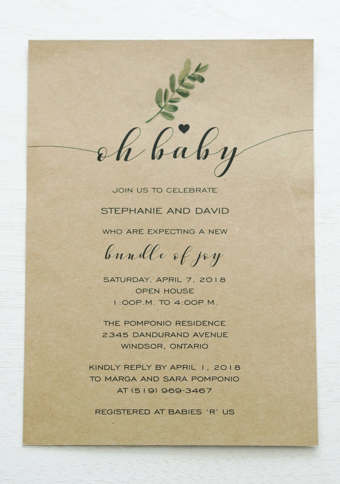 alt=“Simple rustic gender neutral baby shower invitation features kraft card stock with a greenery detail and an “Oh Baby” sentiment with heart”