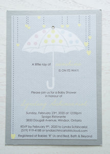 alt=“Adorable gender neutral baby shower invitation features a grey background print and an unbrella image with multicoloured polka dots and hearts with a jewel accent and “A little ray of sunshine is on its way”sentiment mounted onto a silver pearlized shimmer card stock layer”