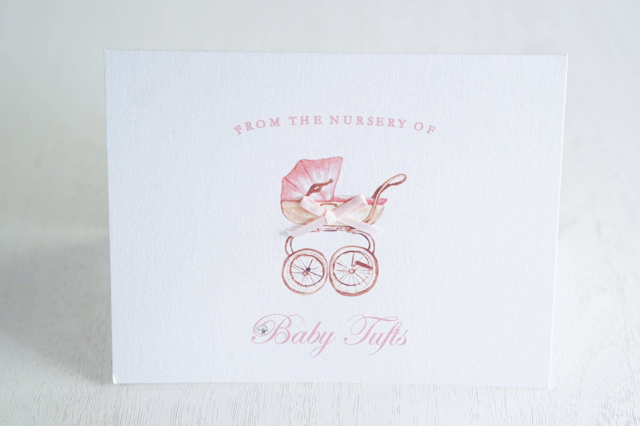 alt=“Sweet baby thank you card features a white pearlescent shimmer card stock, a pink pram with a rich pink satin ribbon bow and a jewel detail”
