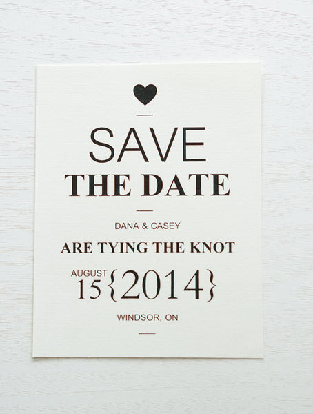 alt="Modern Tying the Knot save the date card is printed on an ivory linen textured card stock and features a heart and your wedding month/day/location in bold fonts"