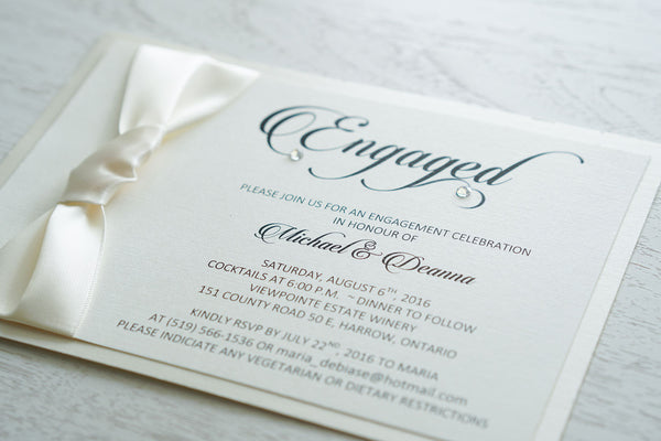 alt="Elegant engagement party invitation features an ivory linen stock on an ivory pearlescent shimmer card stock, a rich ivory ribbon knotted bow and Engaged in script with a jewel detail"