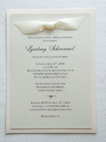 alt="Classic Bridal Shower invitation features an ivory pearlescent shimmer card stock on a blush pink pearlescent stock, an elegant jewel detail and is finished off with a rich satin ivory ribbon bow at the top"