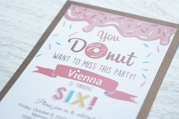 alt="Sweet donut birthday party invitation features a matte white stock on a chocolate brown pearlescent shimmer card stock, a donut and sprinkle design and is finished with a jewel detail"