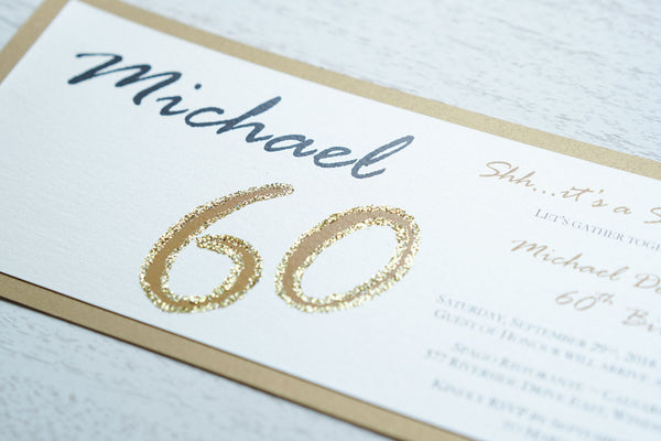 alt=“Modern and fun tea length birthday invitation features an ivory pearlescent shimmer card stock on a gold pearlescent shimmer stock, the honouree’s name in script and their age highlighted with gold glitter sparkle”
