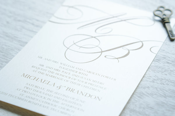 alt="Stylish wedding invitation features an ivory pearlescent shimmer card stock, gold font and a large monogram detail"