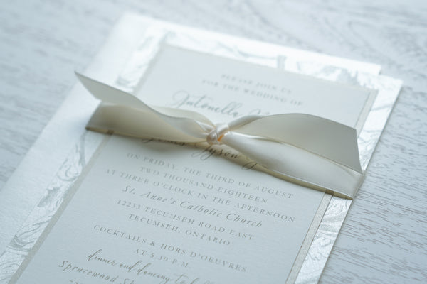 alt="Romantic wedding invitation features ivory matte linen and champagne pearlescent shimmer card stock layered onto a champagne patterned back layer with vintage filigree, scrolls, swirls and etched leaves and is tied together with a a rich ivory satin ribbon"