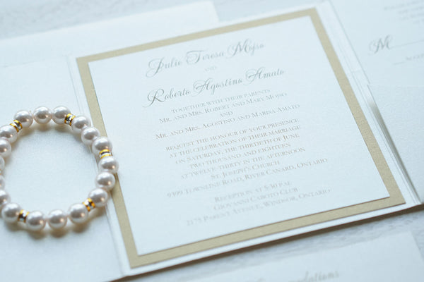 alt="Luxurious ivory pearlescent shimmer square pocket fold wedding invitation features an ivory pearlescent shimmer stock on a gold pearlescent shimmer stock, gold font and a coordinating tab with champagne gold glitter stock layer and a monogram/jewel detail to finish it off"