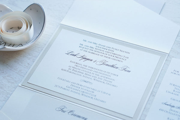 alt="Classic ivory pearlescent shimmer pocket fold wedding invitation features an ivory pearlescent shimmer stock on a champagne gold pearlescent shimmer stock and a coordinating tab with champagne gold glitter layer and a monogram/jewel detail to finish it off"