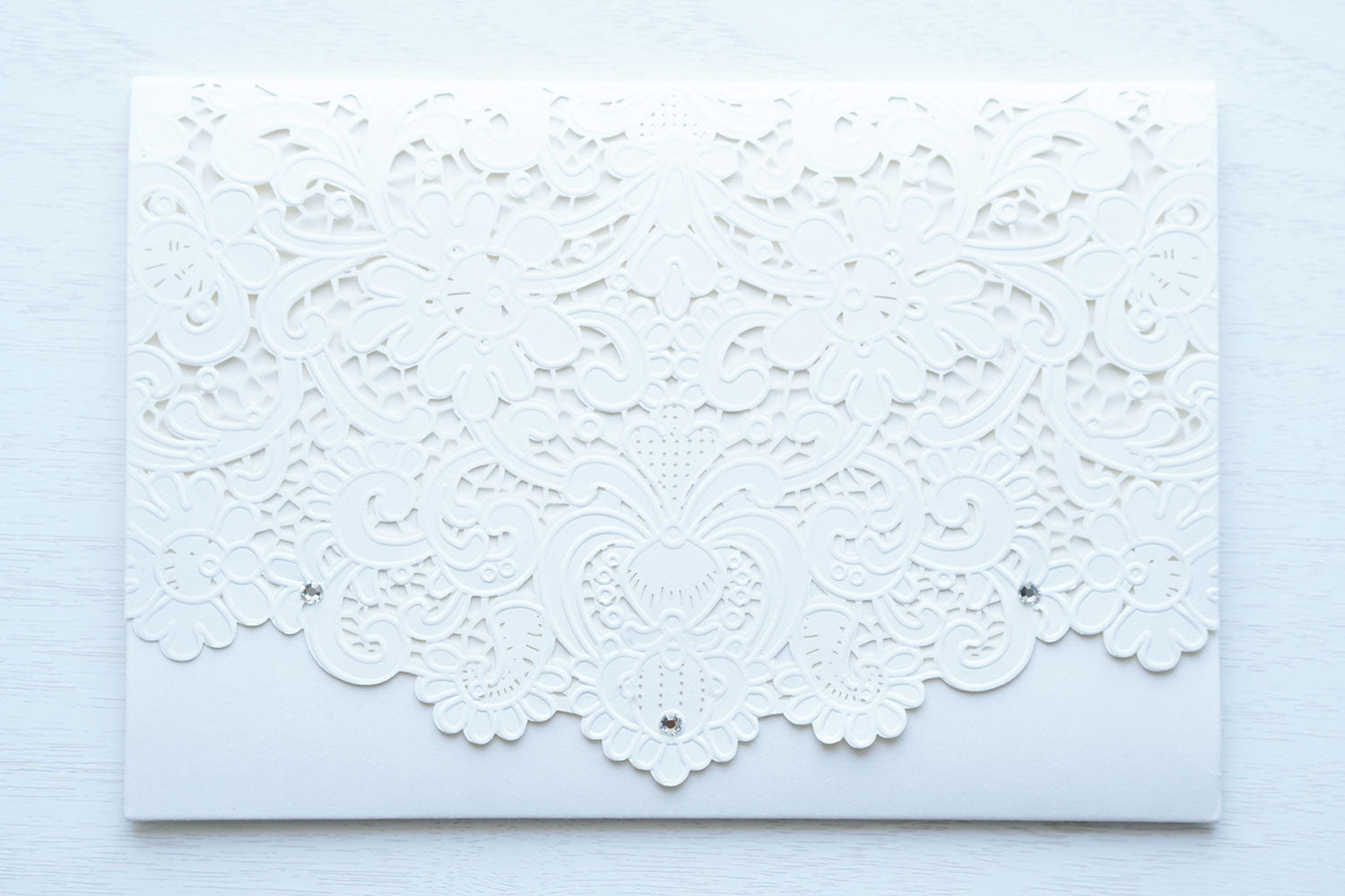 alt="Graceful ivory pearlescent shimmer laser cut pocket fold wedding invitation features an ivory pearlescent shimmer stock on gold mirror and glitter stock layers and encompasses a regal gold frame design with monogram, script font and jewel details"
