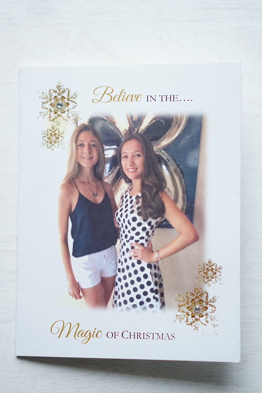 alt="This stylish photo card features a white matte card stock, gold snowflakes with jewels, “Believe in the Magic of Christmas” printed in gold and black writing and a photo of your choice"