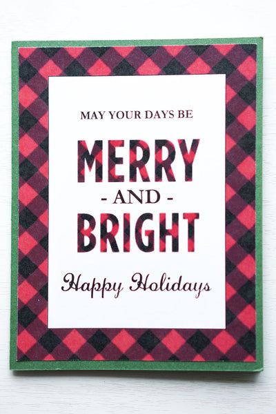 alt=“This modern rustic style card features a white matte card stock on a green pearlescent shimmer card stock, a buffalo plaid pattern and “May your days be merry and bright” printed sentiment with “Happy Holidays” or Merry Christmas” in a script font”