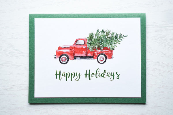 alt="This vintage card features a white matte card stock on a green pearlescent shimmer card stock, a vintage red truck with tree and glitter dust and “Happy Holidays” or "Merry Christmas” in a green script font"