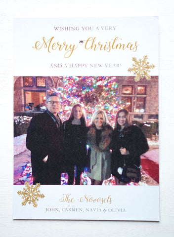 alt="This modern photo card features a white pearlescent shimmer card stock, gold snowflakes with “Wishing you a very Merry Christmas and a Happy New Year” printed in gold and black writing with a jewel detail and includes a photo of your choice"