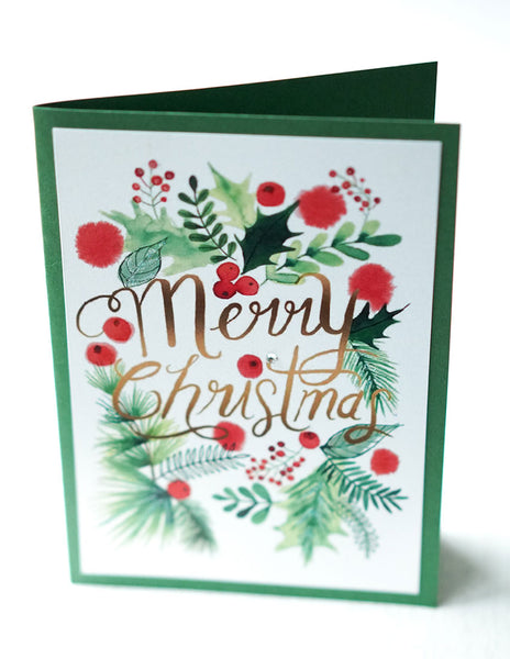 alt="This festive Christmas card features a white and green pearlescent shimmer card stock, watercolour greenery and is finished with glitter dust and a jewel detail"