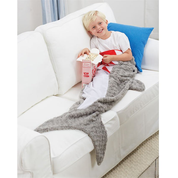 alt="Little boy lounging on the couch with his pillowcase style slide-inside shark blanket which opens at mouth and features swirl, dot and flat minky accents"