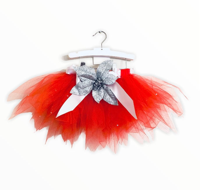 alt="This exclusive Belamour tutu made of the softest high quality red tulle and a rich white satin ribbon, comes embellished with the sweetest silver glitter poinsettia accent and jewels"