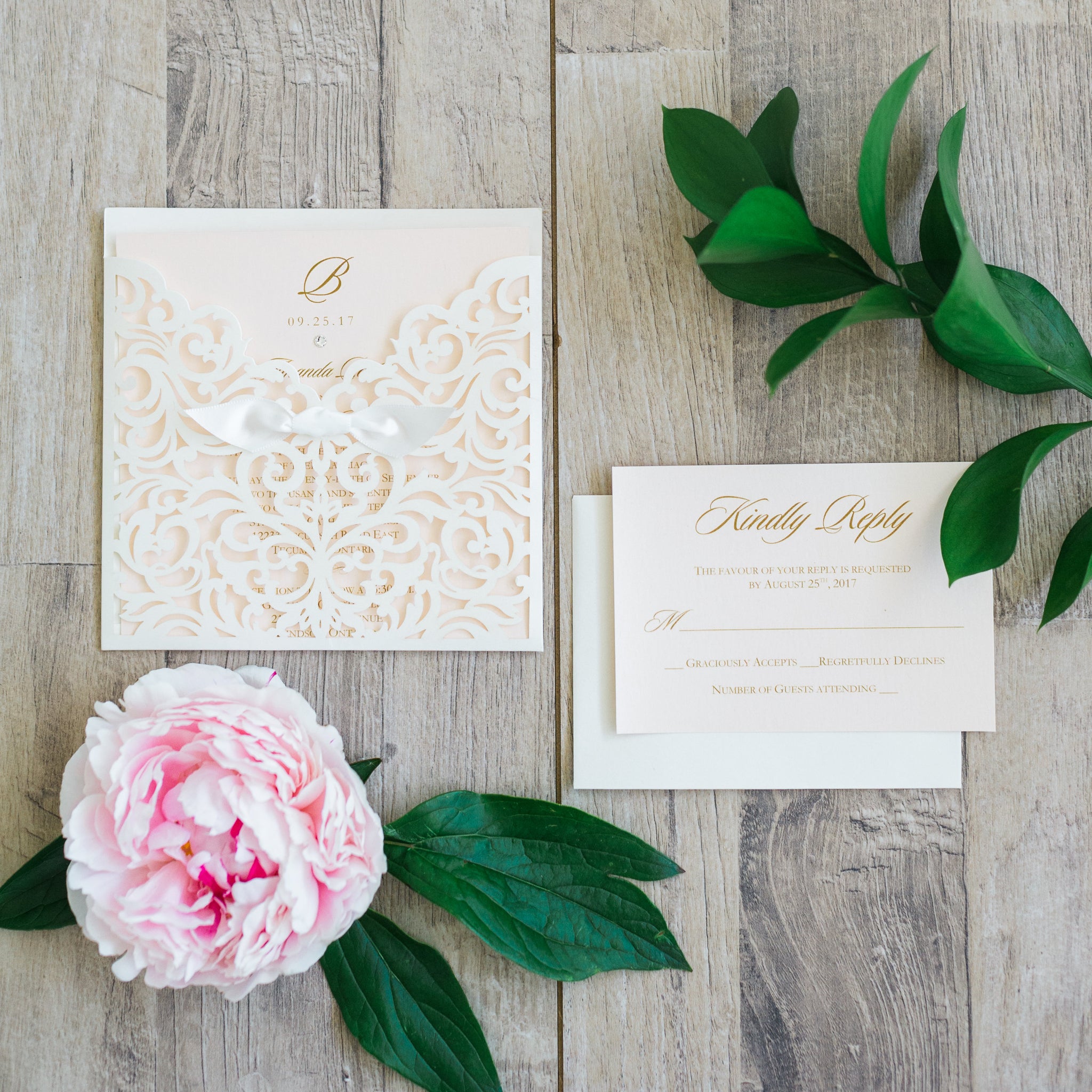 alt="Elegant ivory pearlescent shimmer square pocket laser cut wedding invitation features a rich ivory satin ribbon bow and a soft pink pearlescent shimmer card stock insert with monogram and jewel detail and gold font"