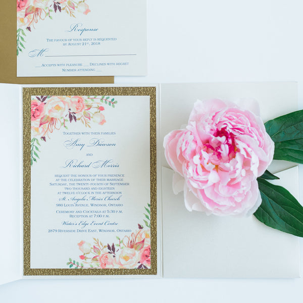 alt="Ivory pearlescent shimmer pocket fold wedding invitation features an ivory pearlescent shimmer stock on a gold glitter stock, a pink watercolour floral design and a coordinating belly band and tab detail"