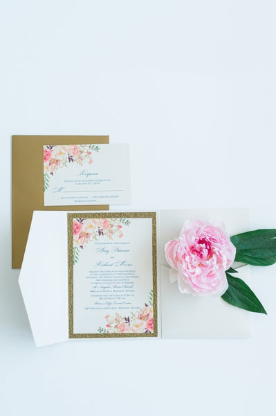 alt="Ivory pearlescent shimmer pocket fold wedding invitation features an ivory pearlescent shimmer stock on a gold glitter stock, a pink watercolour floral design and a coordinating belly band and tab detail"