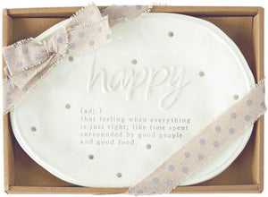 alt=“Oval ceramic plate has a hand-painted polka dot pattern with the word "happy" in raised lettering. The debossed definition says "(adj.) that feeling when everything is just right; like time spent surrounded by good people and good food". Comes in a brown gift box with ribbon tied around”